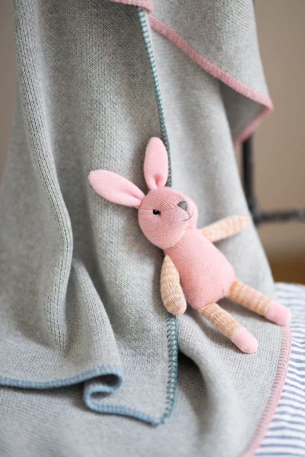 a pink knitted bunny sits on a grey knitted baby blanket